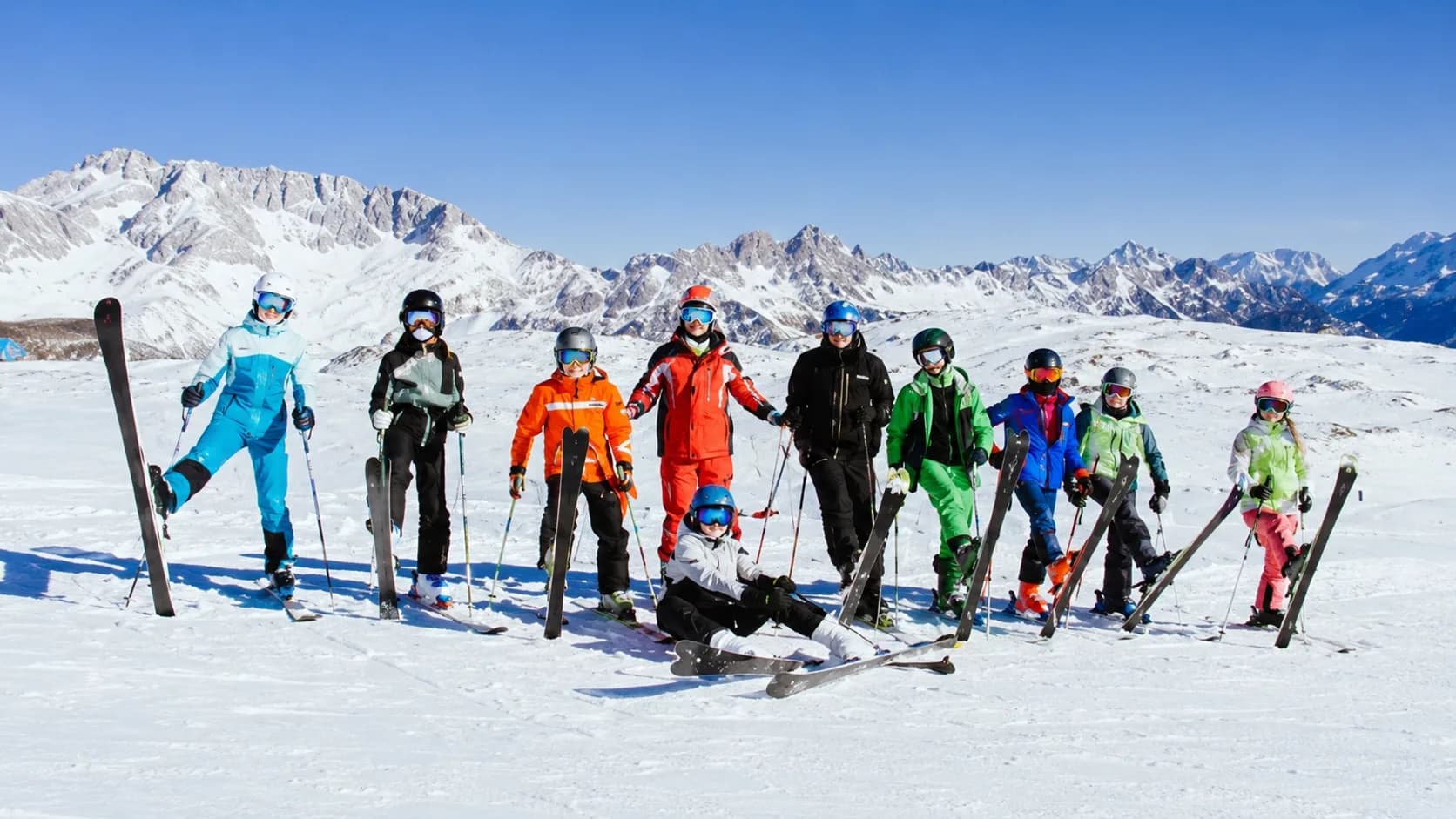 Grupo de niños y jóvenes con esquís en la cima de una montaña nevada